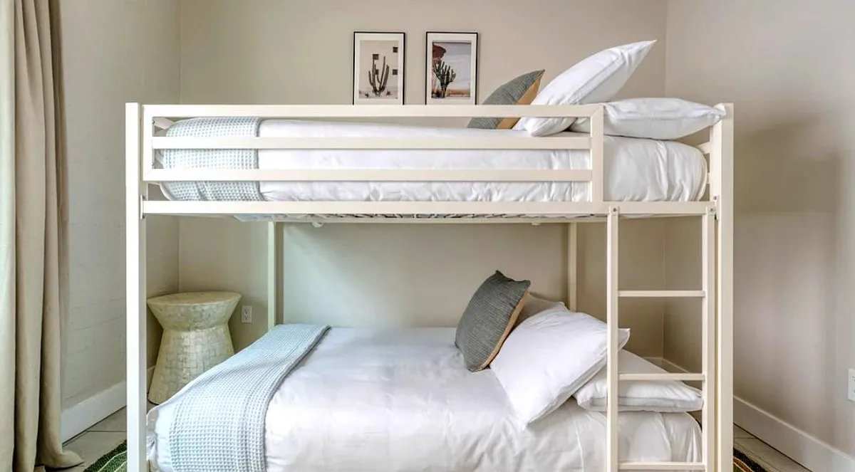 A cozy kids' bedroom featuring a bunk bed with decorative pillows, playful framed artwork, and a textured blanket. The room radiates comfort and is clearly set up for young children to feel at home.